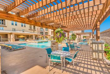A wooden pergola over a poolside seating area.